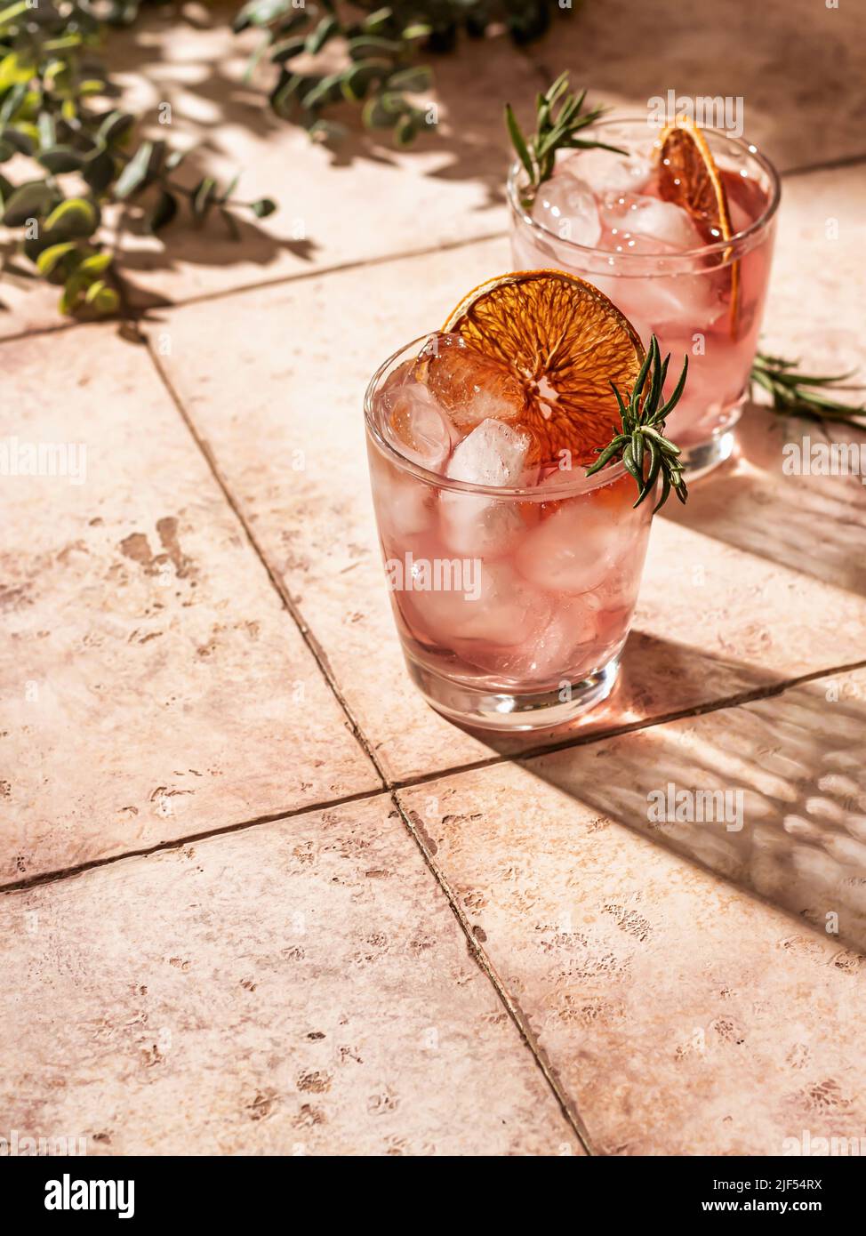 Cocktails d'été glacés à l'orange séché avec romarin et superbes ombres sur fond de carreaux. Orientation verticale. Espace de texte Banque D'Images
