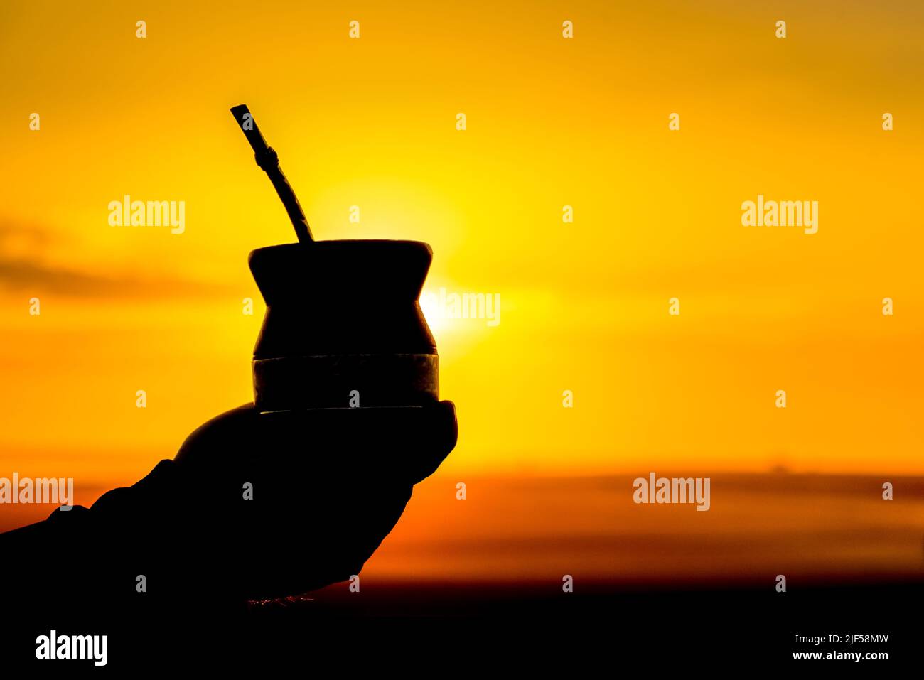 Silhouette d'une main tenant un verre de yerba mate au coucher du soleil doré Banque D'Images