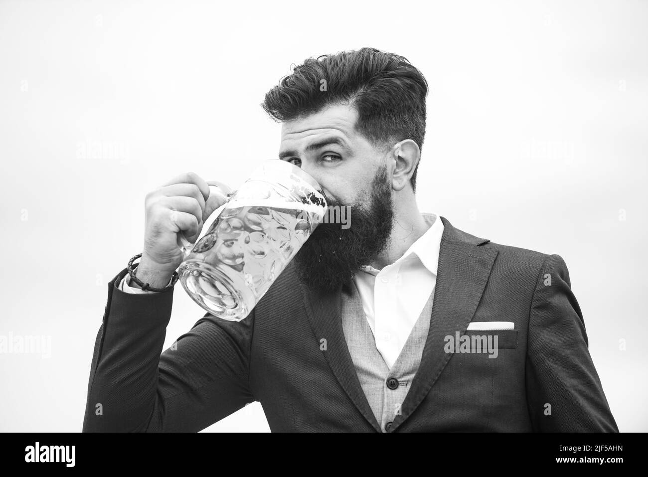 Homme en costume classique buvant de la bière. Un homme barbu dans une tenue classique est heureux et satisfait. Portrait de l'homme avec un verre de bière levé. Banque D'Images