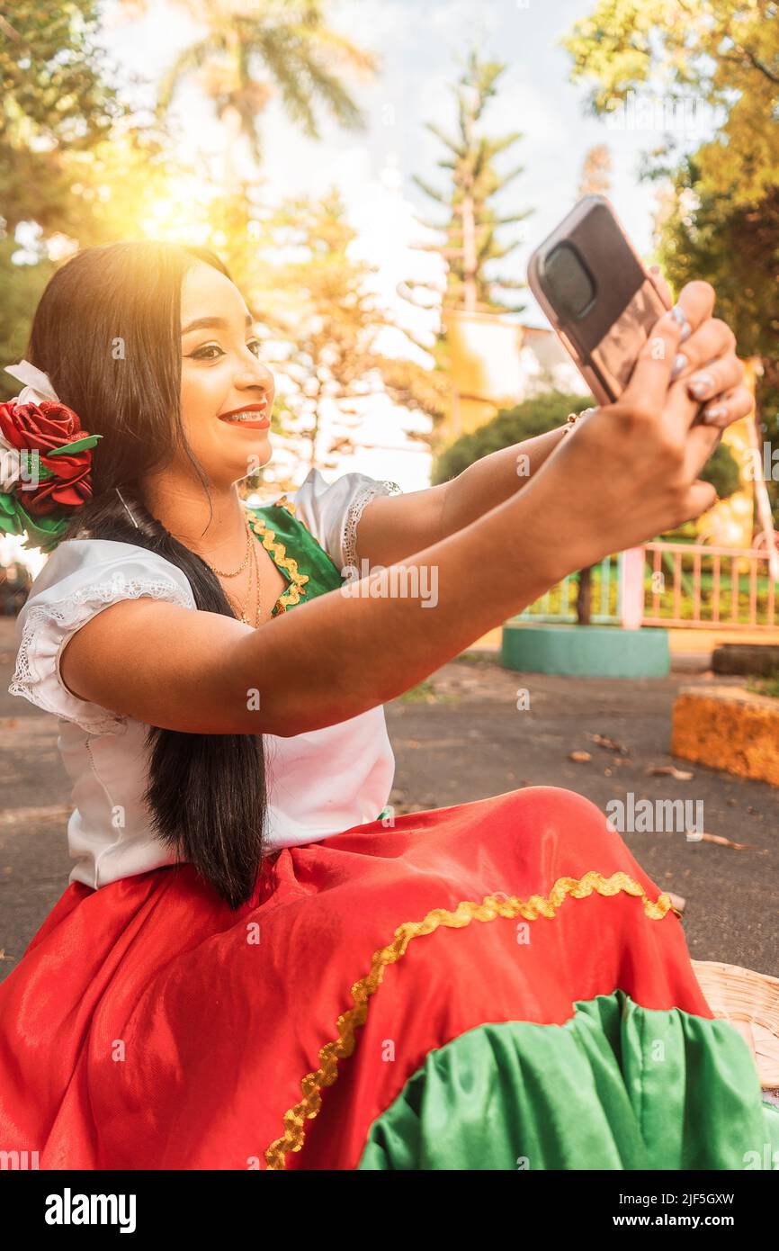 Magnifique adolescent latin en robe traditionnelle prenant un selfie dans un parc pendant une journée ensoleillée Banque D'Images
