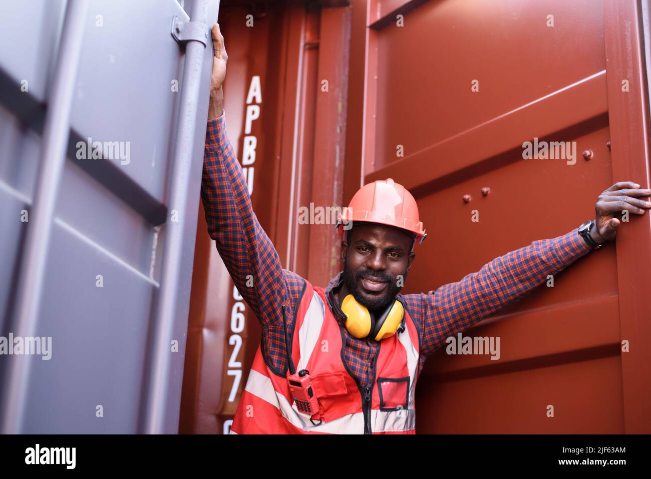 Joyeux ingénieur afro-américain souriant lorsqu'il se tient à l'entrepôt de conteneurs, Worker obtient la sécurité sociale et l'assurance, la fête du travail et le succès Banque D'Images