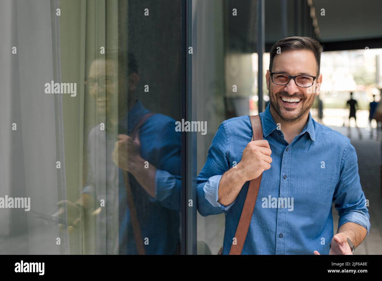 Portrait d'un homme d'affaires souriant portant un sac pour ordinateur portable. Un jeune homme professionnel porte des formes. Il est debout près de la fenêtre de l'immeuble de bureaux de l'ec Banque D'Images