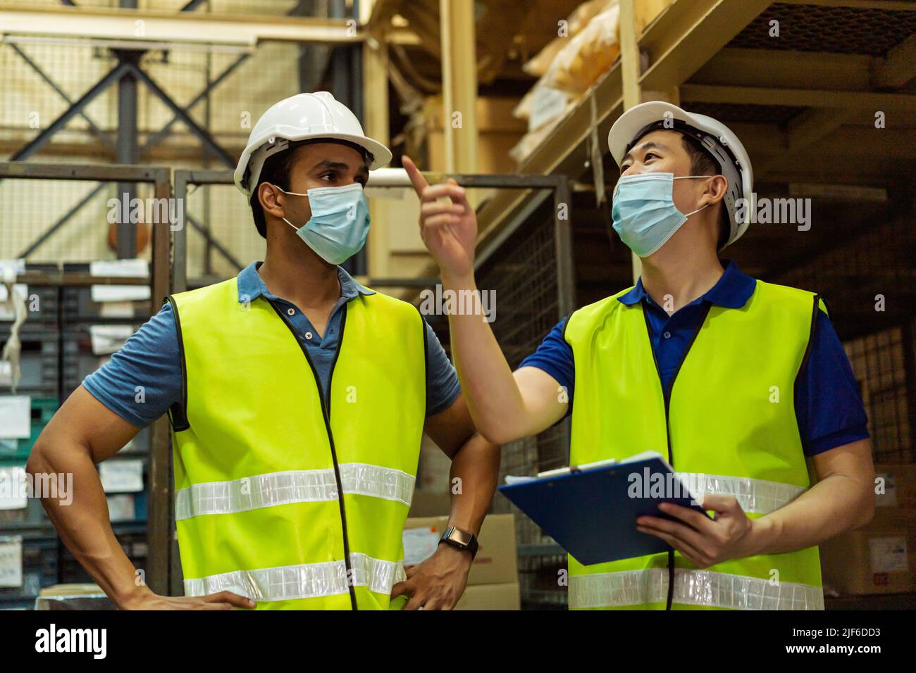 Groupe de jeunes travailleurs d'entrepôt d'usine portant un masque de protection tout en travaillant dans l'industrie logistique intérieure. Des hommes de souche asiatique et indienne vérifient la commande d'articles pendant la pandémie de coronavirus Covid 19 Banque D'Images