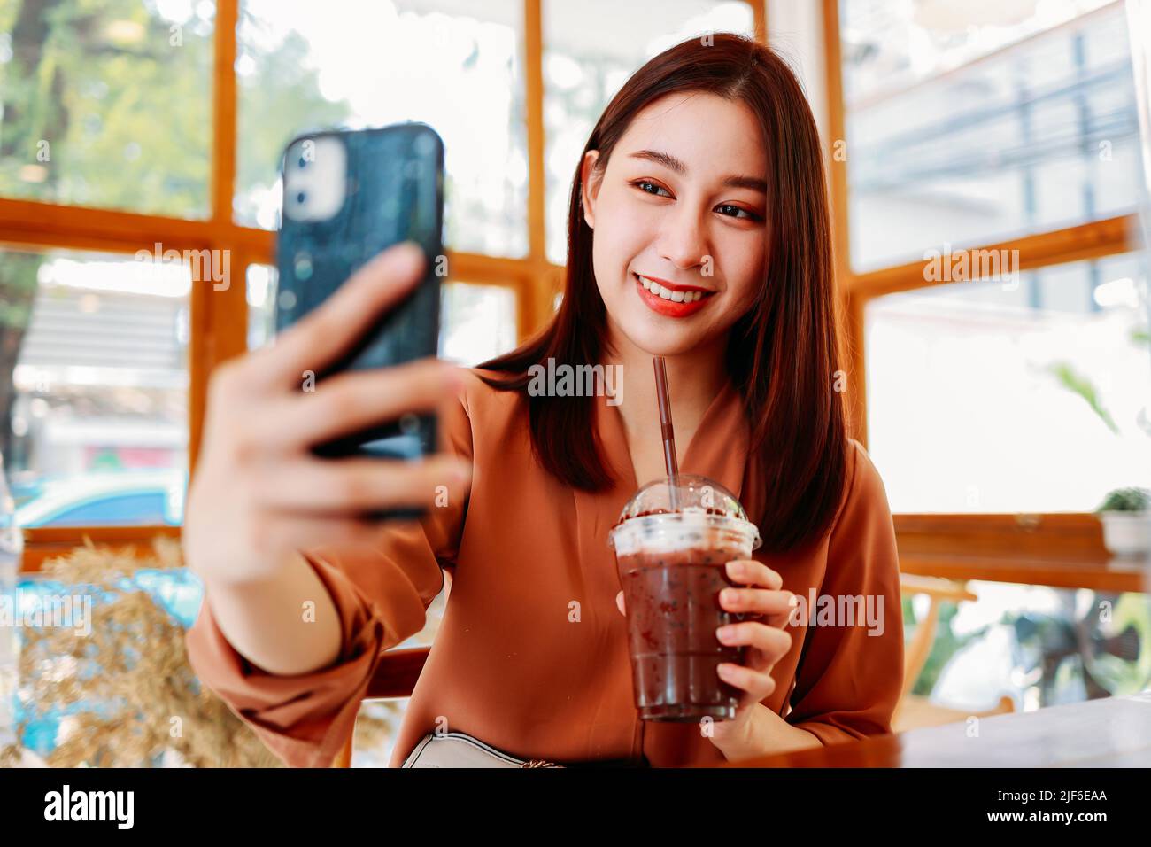 Jeune femme asiatique blogueuse de nourriture prenant selfie avec smartphone tenant un verre de cacao frais tout en étant assise dans un café avec social distancer pendant le coronavirus Banque D'Images