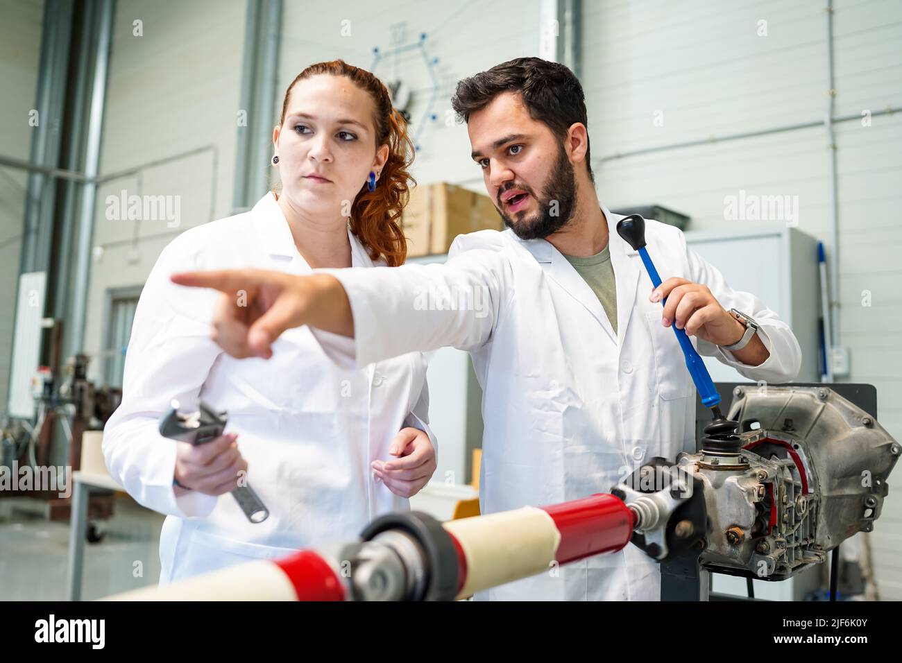 Scientifique en uniforme médical pointant vers l'extérieur près d'une collègue femelle debout avec une clé près d'un équipement spécial avec tube métallique pendant le processus de réparation dans Banque D'Images