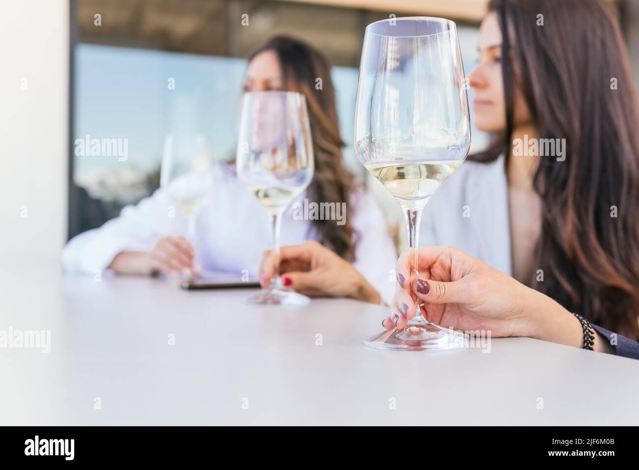 Pantacourt non reconnaissable de brunettes ethniques adultes dans des vêtements élégants et décontractés avec des verres de vin blanc assis à table ronde le week-end sur le restaurant Banque D'Images