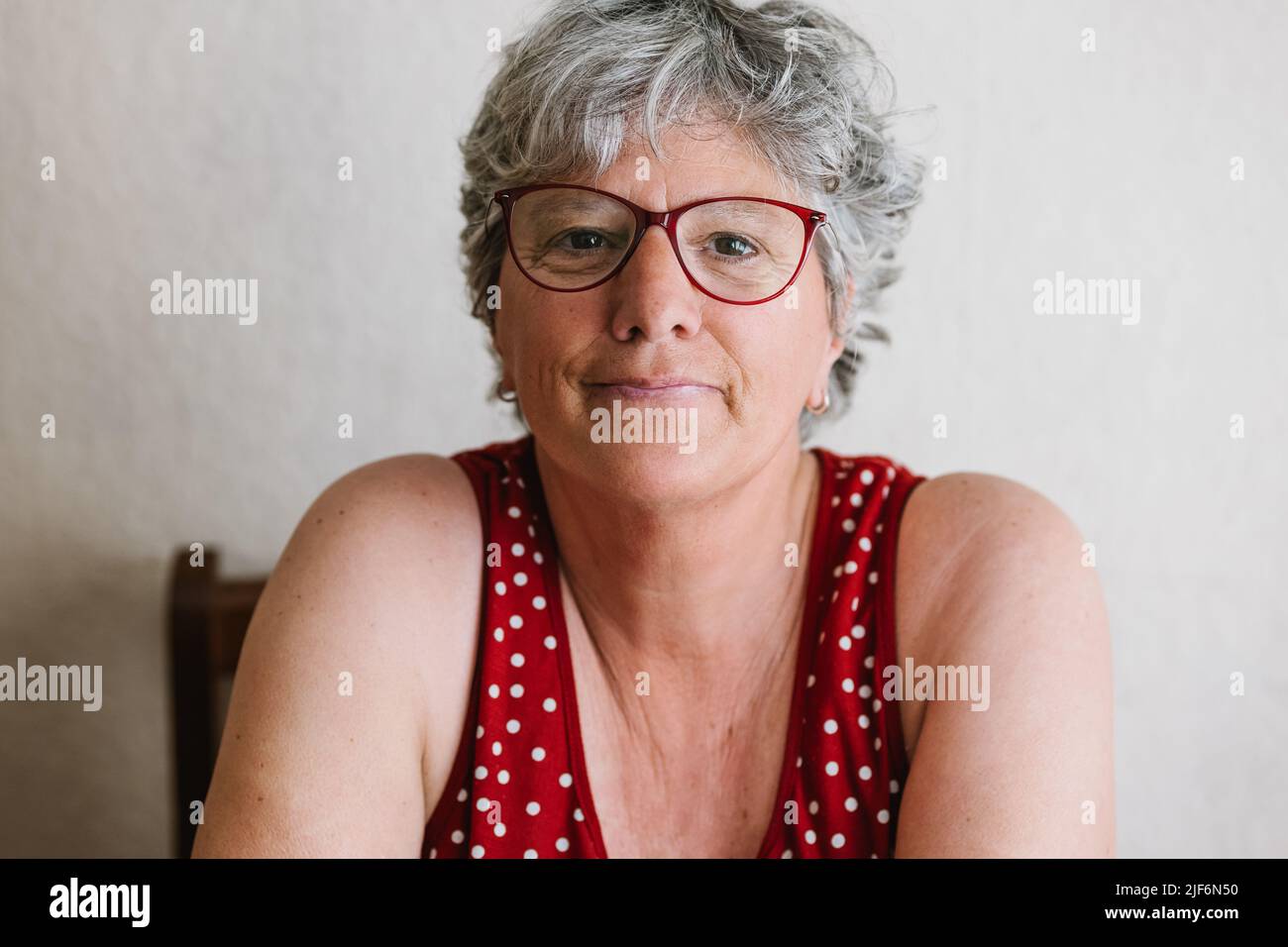 Femme âgée positive avec des cheveux gris dans des vêtements décontractés et des lunettes souriant et regardant l'appareil photo Banque D'Images