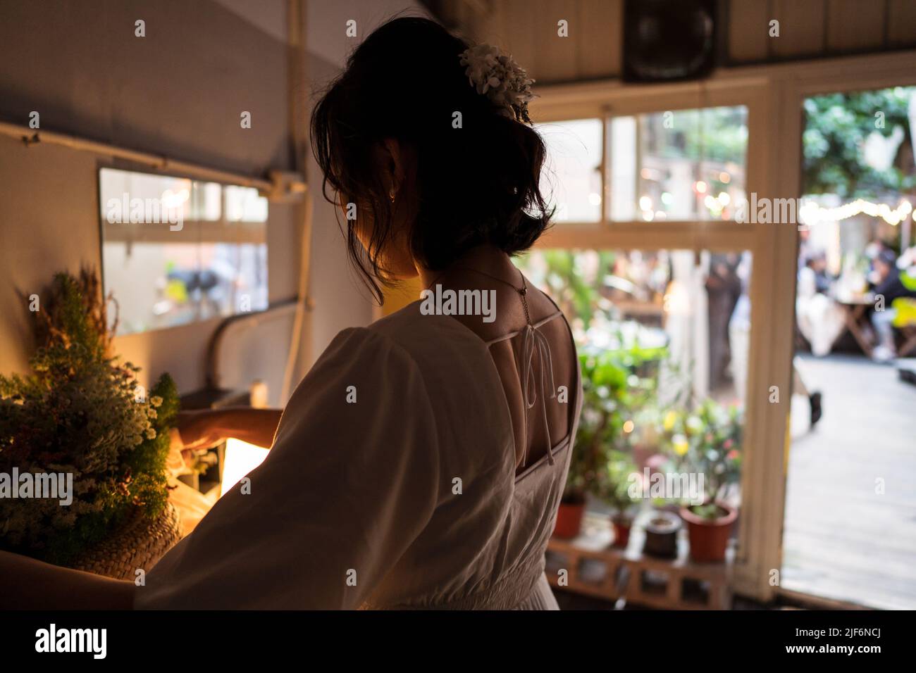 Vue arrière de la jeune mariée en robe blanche regardant le bouquet de fleurs et préparant pour la célébration de mariage dans la chambre confortable Banque D'Images