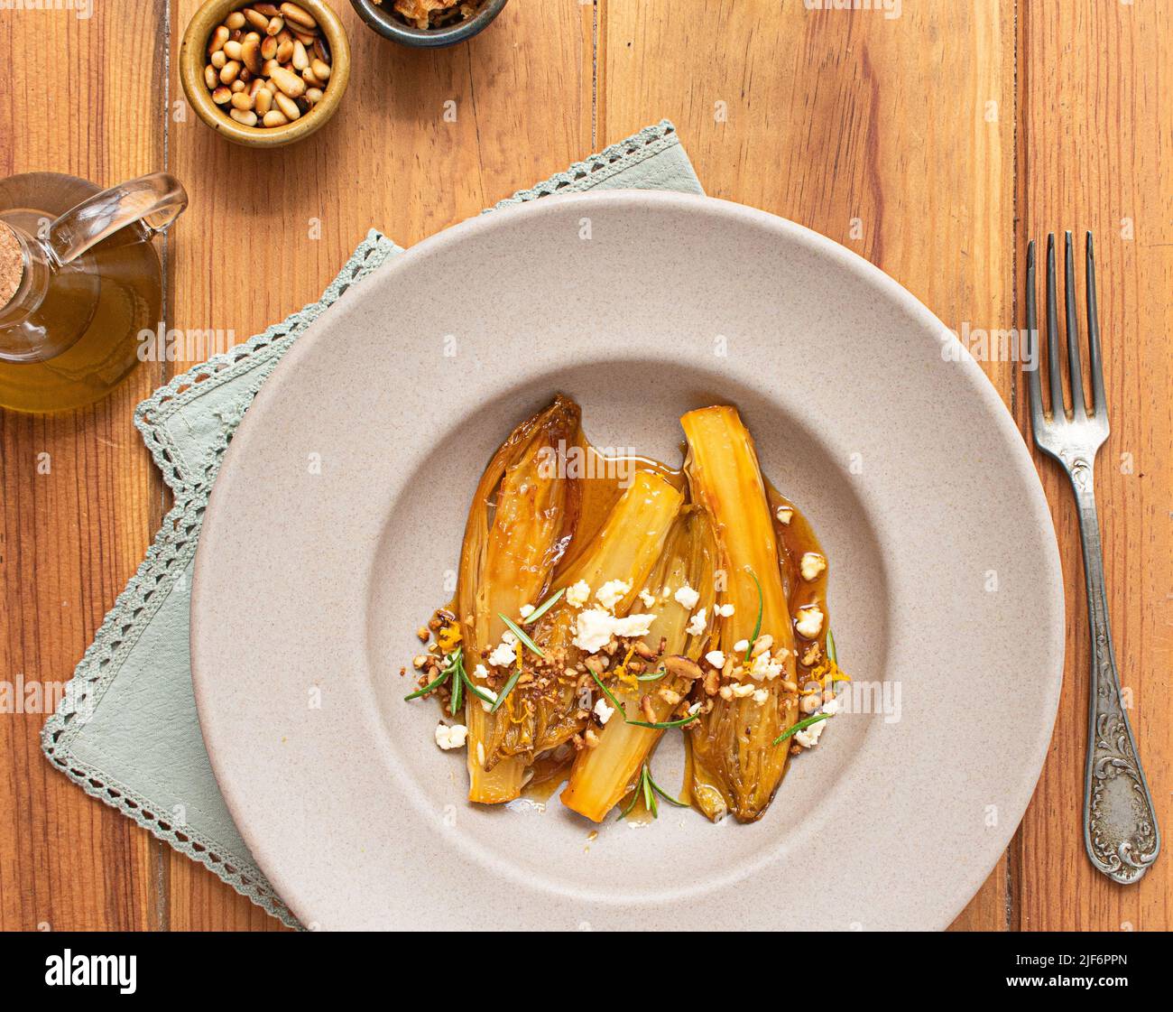 Vue de dessus des endives braisées avec jus d'orange sur une table en bois à côté d'une fourchette et différents bols Banque D'Images