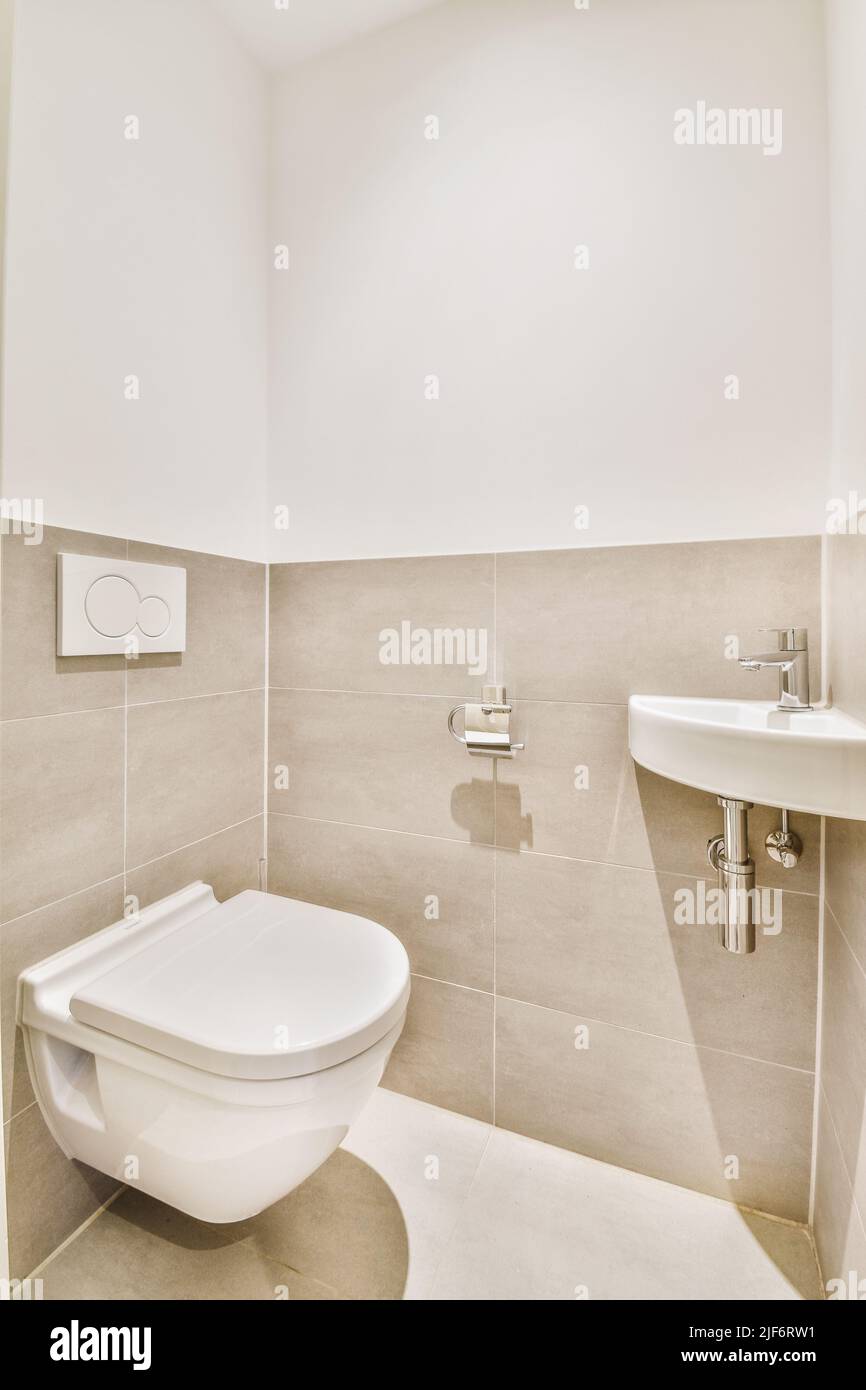 toilettes murales et petit lavabo dans le coin des toilettes chambre avec carrelage beige Banque D'Images