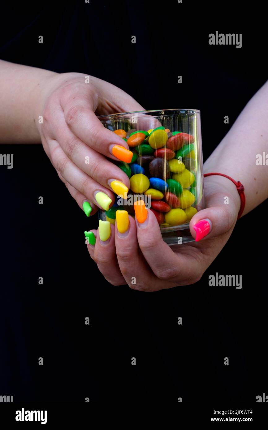 femme avec des extensions d'ongle peintes dans une variété de couleurs tenant le verre rempli de bonbons colorés Banque D'Images