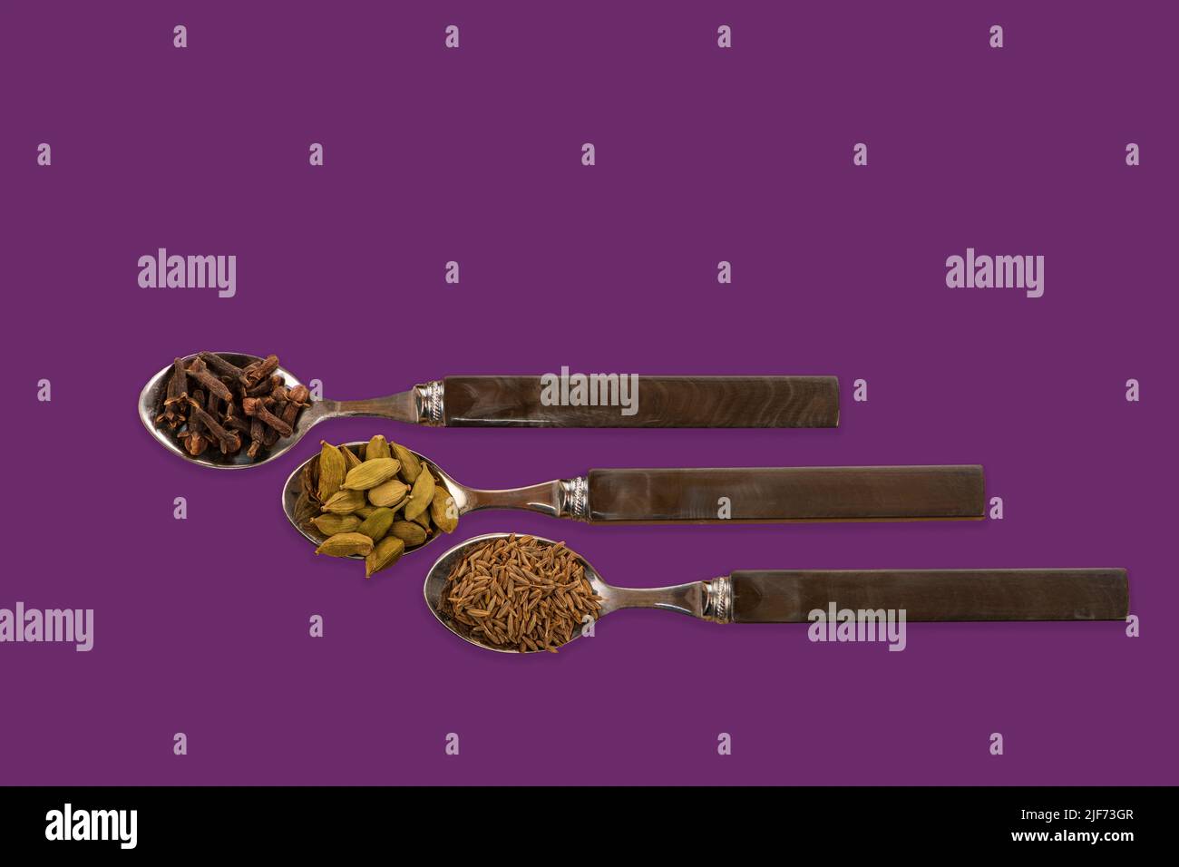 Image de concept avec des cuillères contenant des graines de cumin de clous de girofle et des gousses de cardamon sur un fond violet coloré Banque D'Images