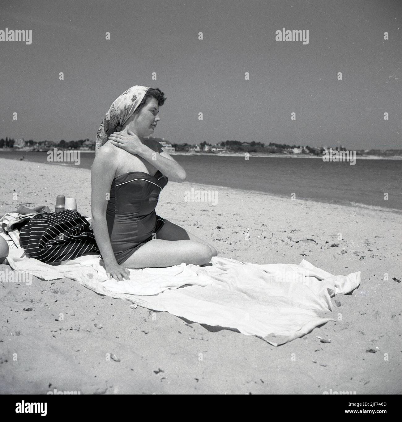 1950s, historique, une femme dans un maillot de bain de l'époque, avec un foulard, assis sur une serviette sur une plage de sable, Angleterre. ROYAUME-UNI. Banque D'Images