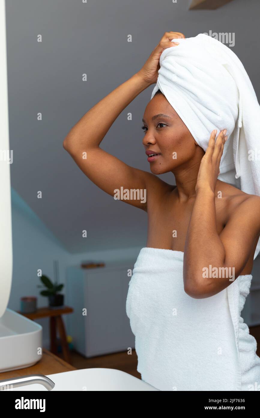 Jeune Afro-américaine ajustant sa serviette blanche dans la salle de bains à la maison, espace de copie Banque D'Images