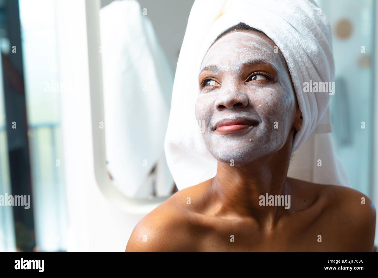 Gros plan de la jeune femme afro-américaine avec la crème de visage appliquée regardant loin, espace de copie Banque D'Images