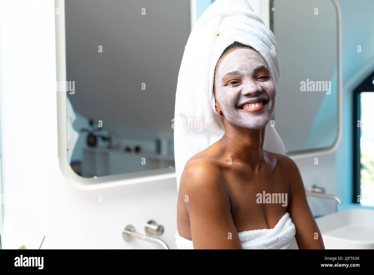Portrait de jeune femme afro-américaine joyeuse avec crème visage sur le visage dans la salle de bains, espace copie Banque D'Images