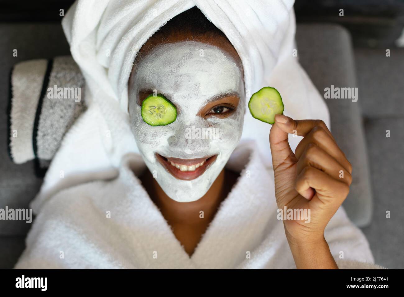 Portrait de jeune femme afro-américaine souriante avec crème pour le visage, tranches de concombre sur le visage relaxant Banque D'Images