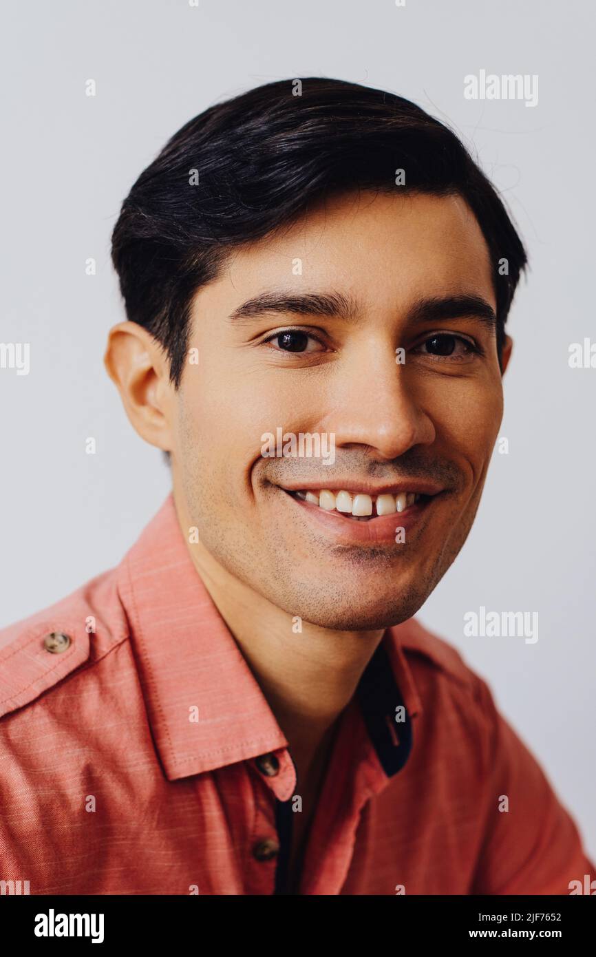 Headshot hispanique latino homme noir cheveux souriant beau jeune adulte portant une chemise de melon sur fond gris regardant la prise de vue en studio Banque D'Images