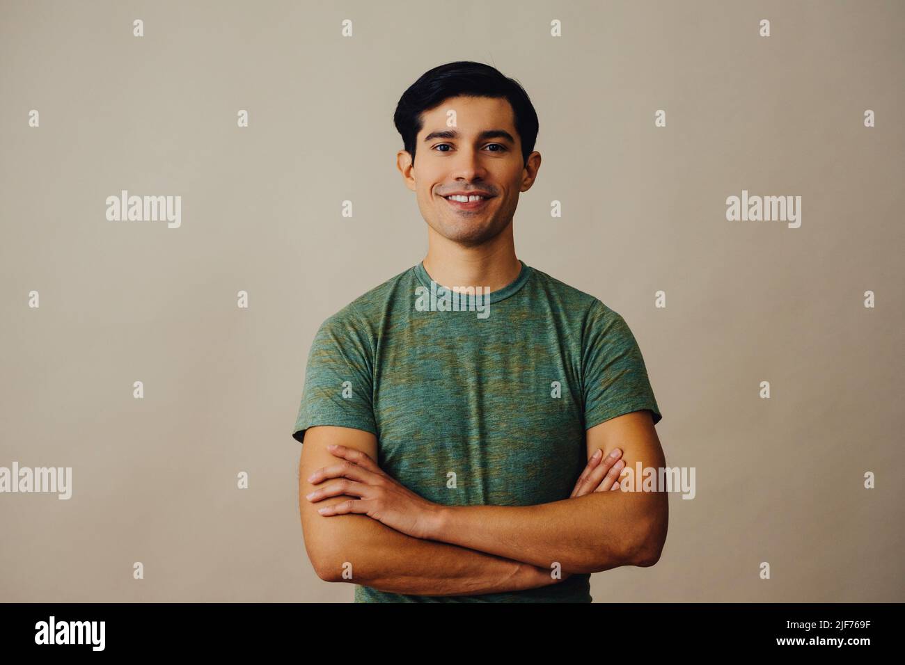Portrait hispanique latino-homme avec les bras croisés et les cheveux noirs souriant beau jeune adulte vert t-shirt sur fond gris regardant la prise de vue en studio d'appareil photo Banque D'Images