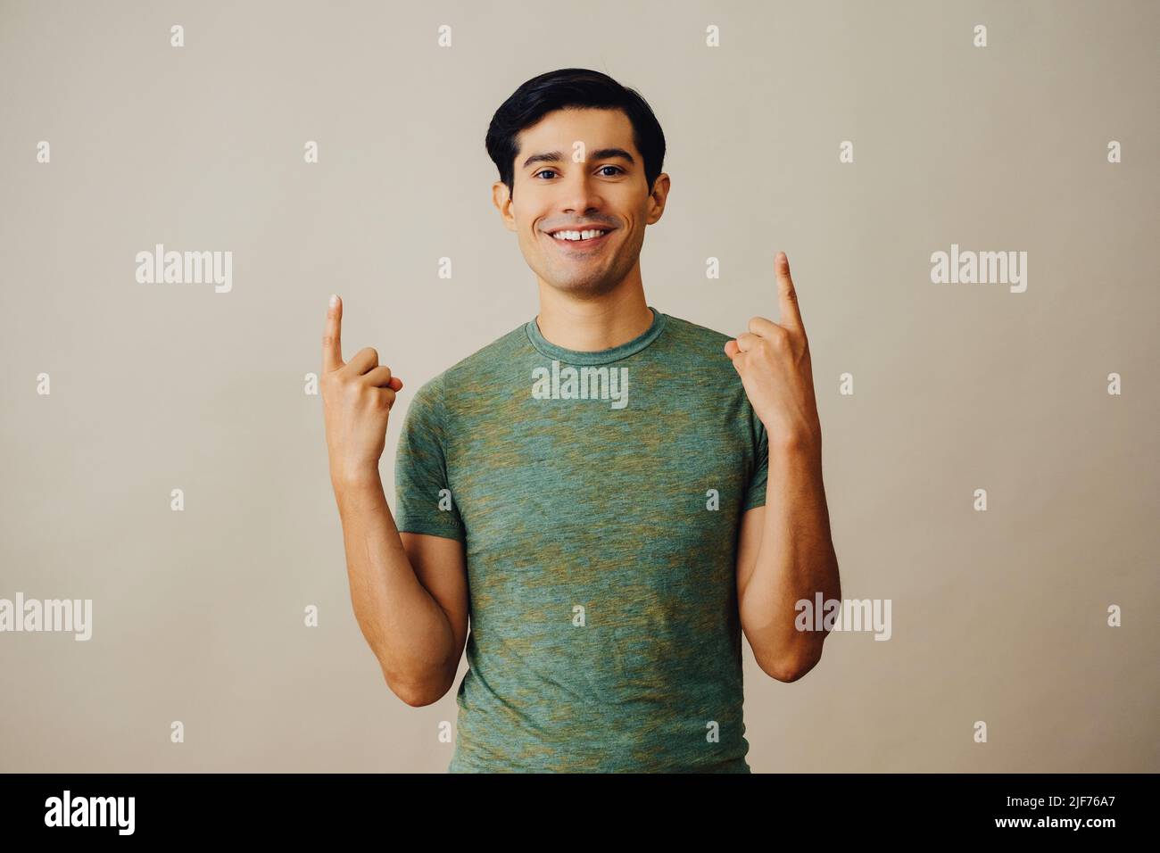 Portrait hispanique latino homme pointant vers le haut cheveux noirs souriant beau jeune adulte vert t-shirt sur fond gris regardant la prise de vue en studio Banque D'Images