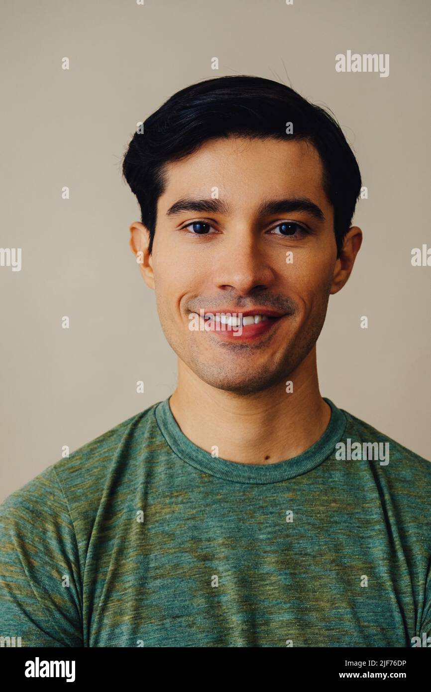 Headshot latino homme noir cheveux souriant beau jeune adulte vert t-shirt sur fond gris regardant la prise de vue en studio Banque D'Images