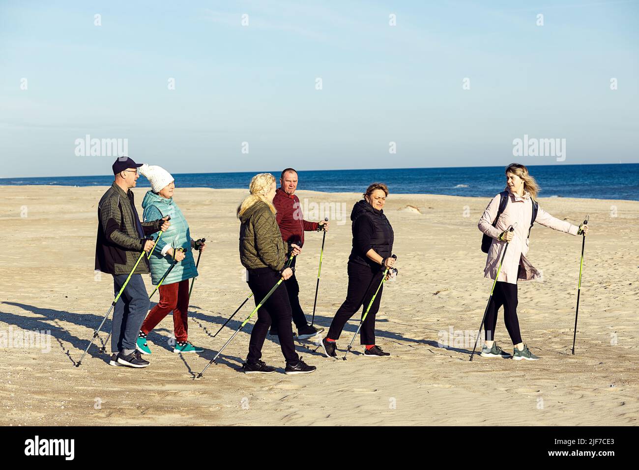 Leader sportswoman, entraîneur et groupe de personnes joyeux marche scandinave avec des bâtons à la plage de sable près de la mer. Copier l'espace Banque D'Images