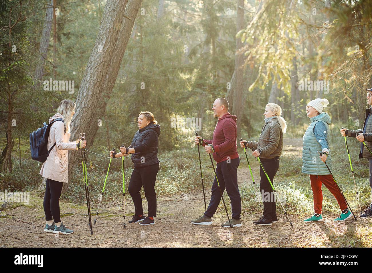 Femme blonde avec groupe de personnes enseigner le jogging scandinave, exercices de forme physique avec des bâtons dans les bois, expliquer les règles Banque D'Images