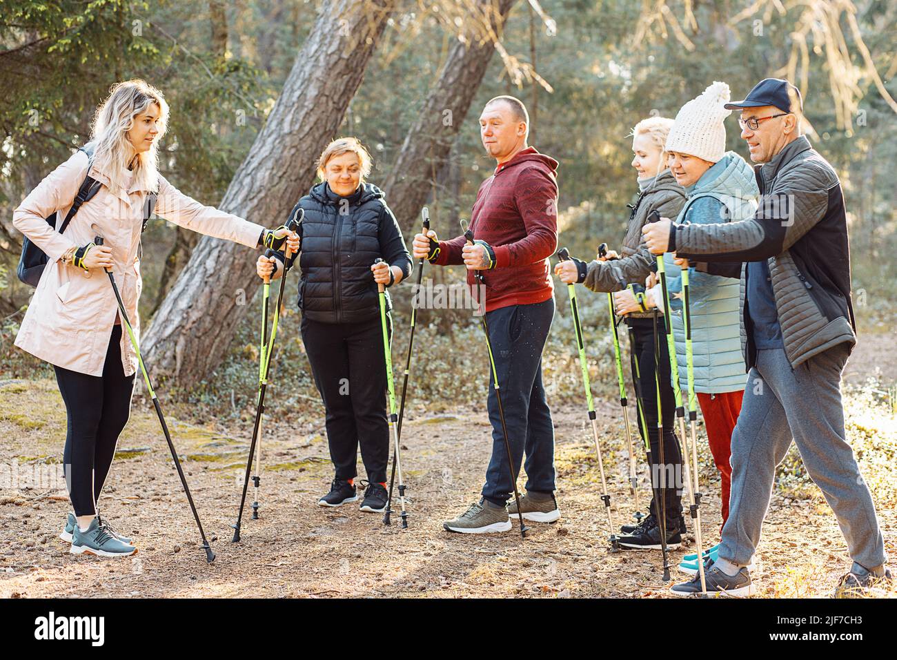 Une entraîneuse sportive sérieuse avec un groupe de personnes parlant, expliquant la posture pour la marche nordique avec des bâtons dans la forêt Banque D'Images