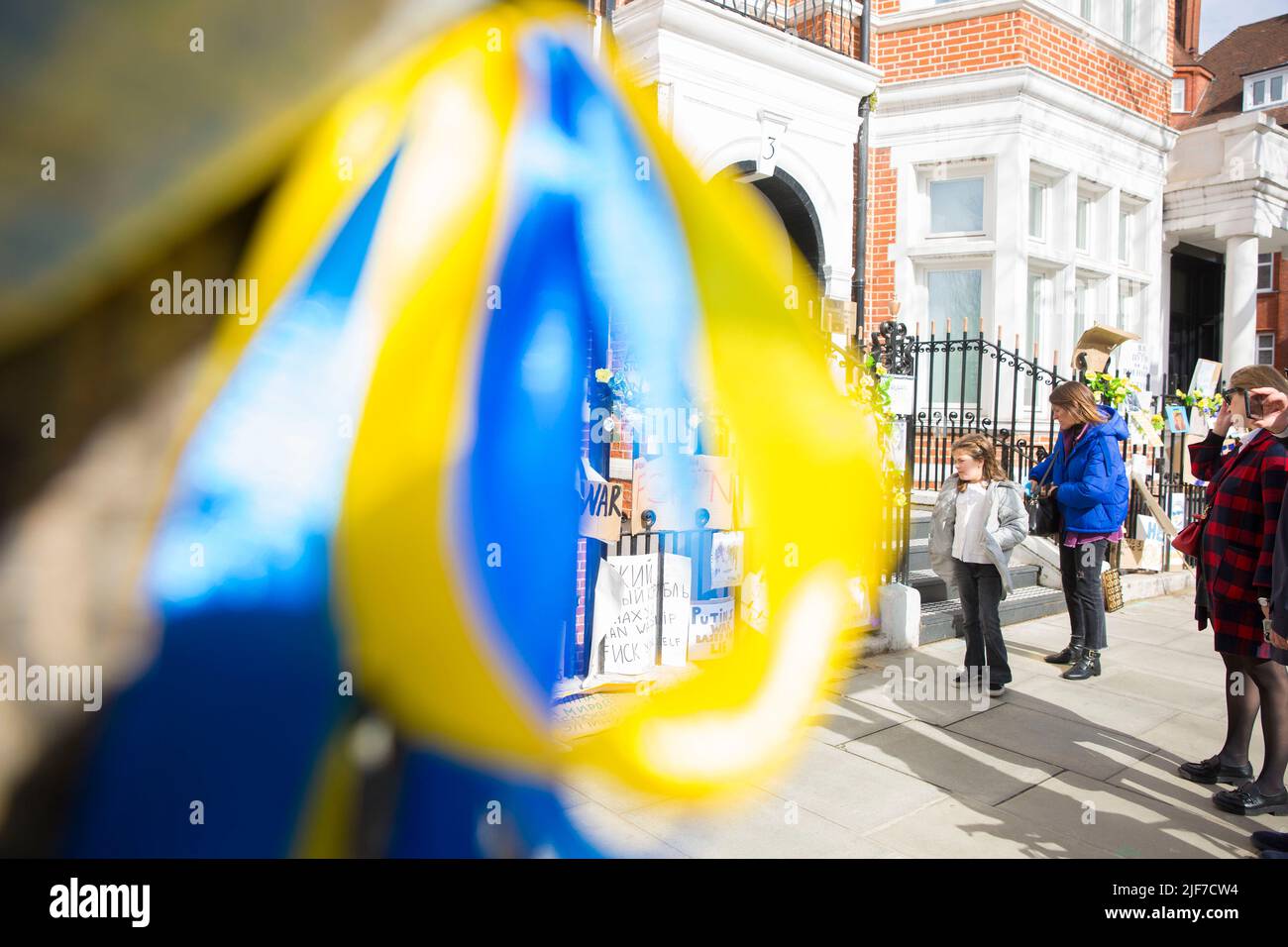 Derrière des rubans bleus et jaunes attachés à un arbre, des messages et des affiches contre l’invasion de l’Ukraine par la Russie sont laissés près de l’ambassade de Russie à Londres. Banque D'Images