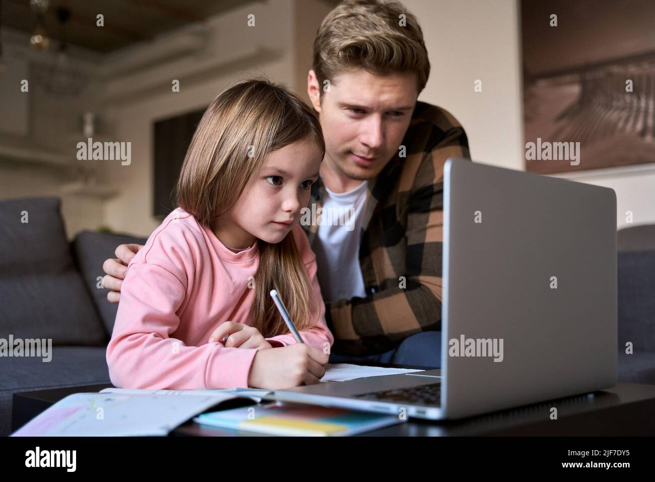 Enfant fille apprenant un cours virtuel en ligne sur appel vidéo avec papa à la maison. Banque D'Images