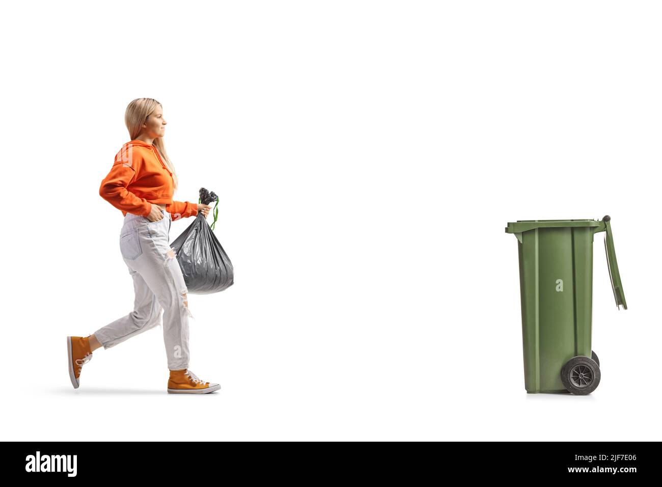 Photo pleine longueur d'une jeune femme transportant un sac de déchets en plastique et se rapprochant d'un bac isolé sur fond blanc Banque D'Images