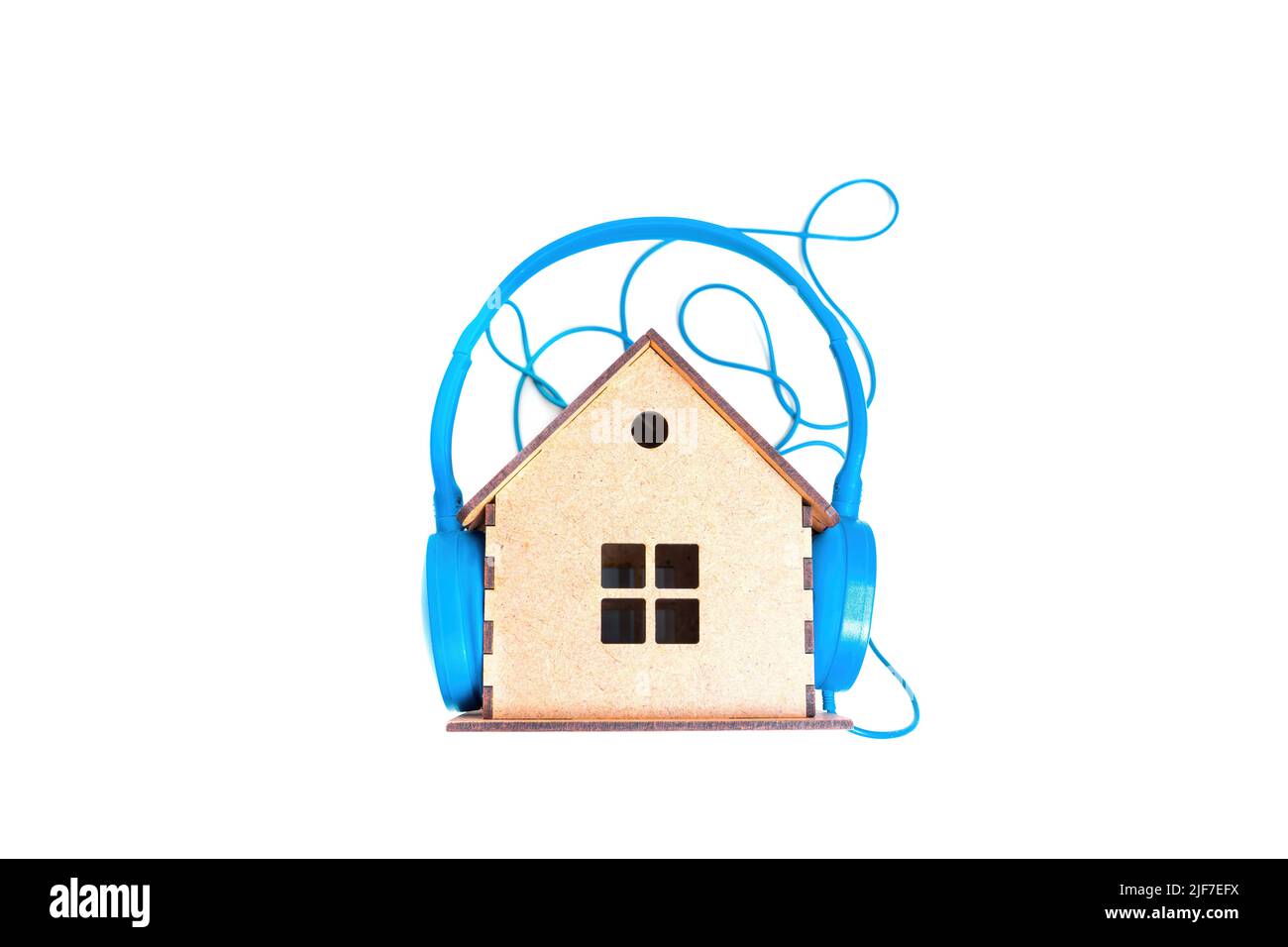 Casque filaire bleu clair placé sur une petite maison en bois isolée sur fond blanc. Concept d'isolation acoustique créatif. Banque D'Images