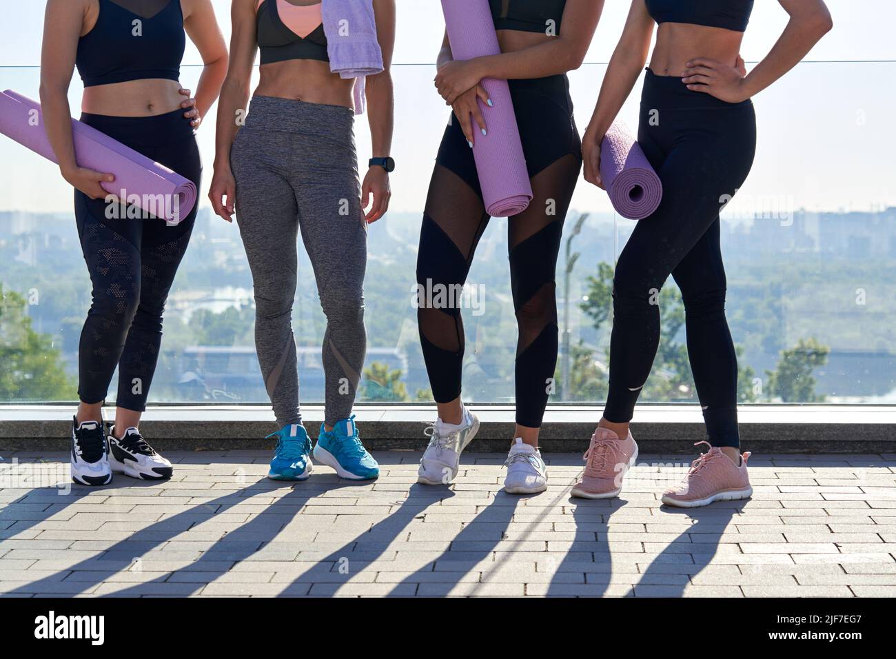 Tenue sportive femmes amis vêtements de sport tenir les tapis de yoga tenir debout ensemble à l'extérieur. Banque D'Images