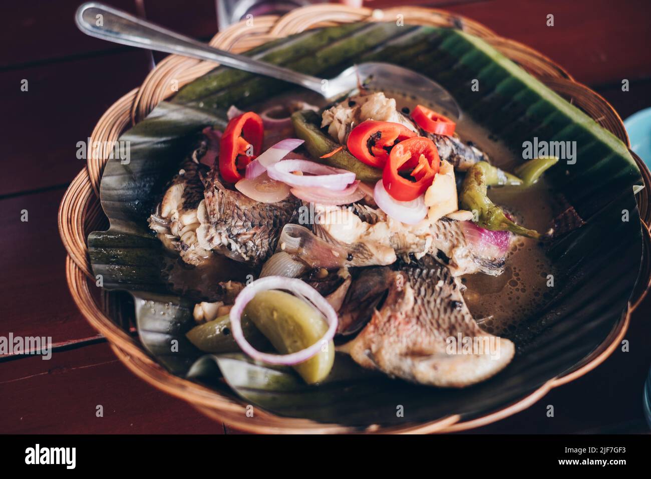Service de plat philippin Tilapia poisson simmered dans le vinaigre et les épices sur la feuille de banane sur plaque en rotin bois. Mise au point sélective. Banque D'Images