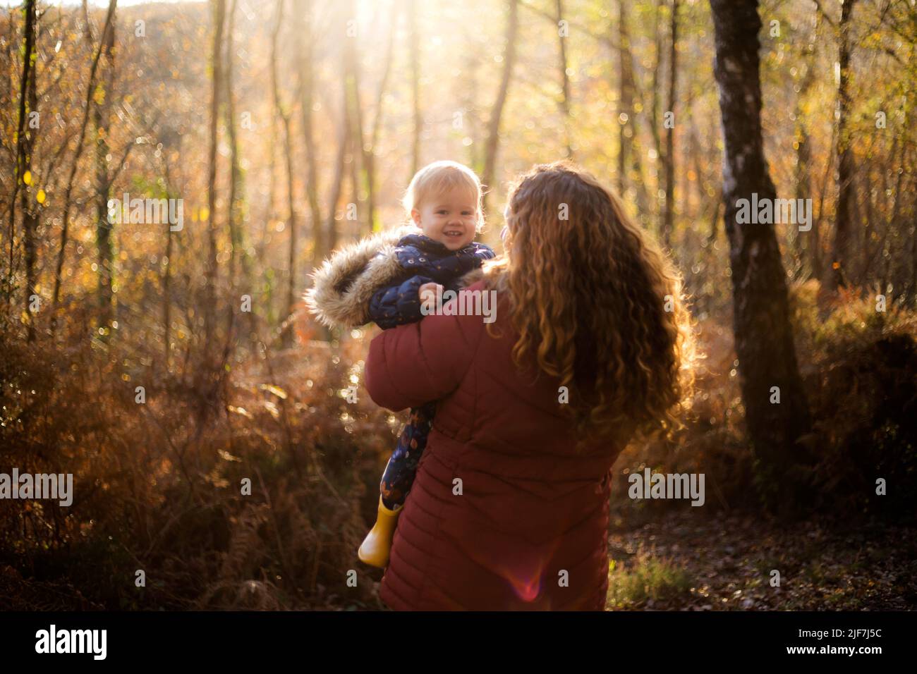 une femme aux cheveux rouges de curley tenant un bébé souriant dans une forêt Banque D'Images