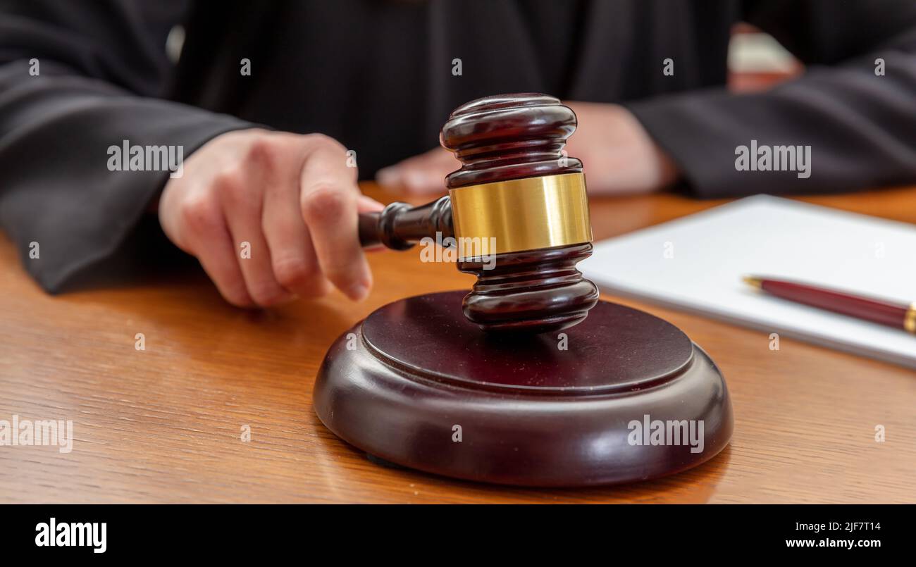 Main féminine tenant une loi de vente aux enchères gavel. Femme juge avec un bloc-notes frappant un maillet en bois, vue rapprochée. Banque D'Images