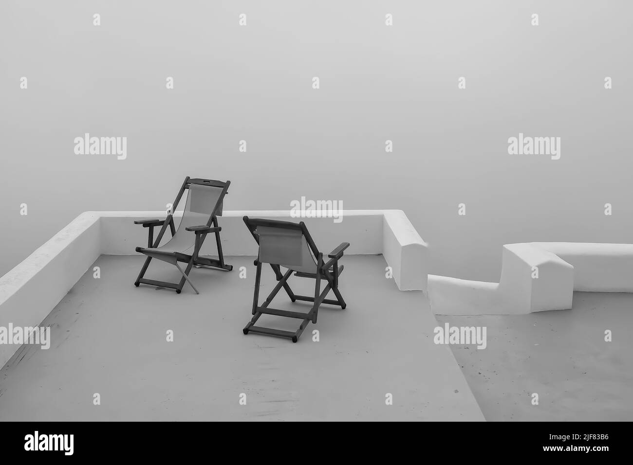 Vue sur deux chaises longues vides en face de la mer égée qui est couverte de brouillard à Santorini Grèce en noir et blanc Banque D'Images