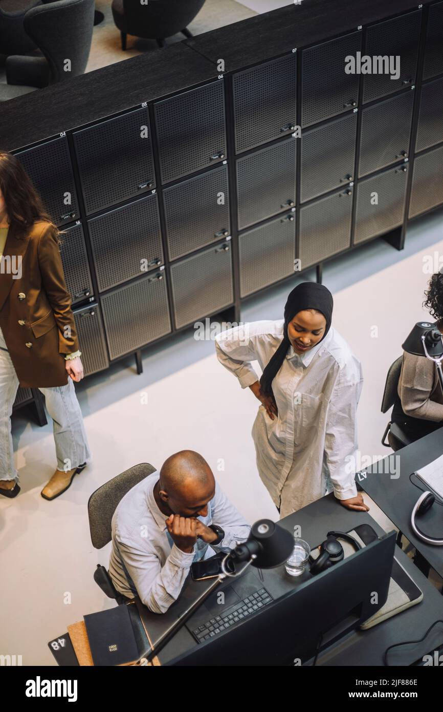 Vue en grand angle d'une jeune femme d'affaires debout à la main sur la hanche discutant avec un collègue assis à son bureau Banque D'Images