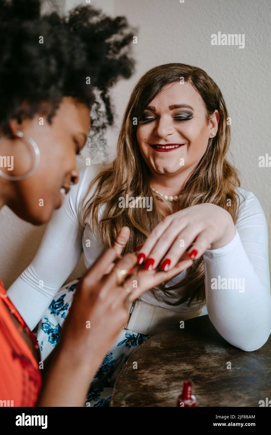 Jeune femme appliquant vernis à ongles à un ami non binaire à la maison Banque D'Images