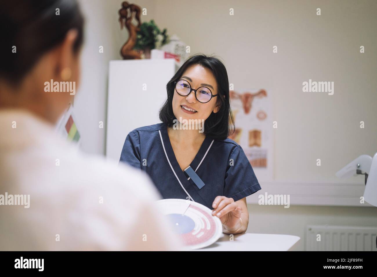 Une femme souriante présente un tableau de fécondation in vitro tout en discutant avec le patient en clinique Banque D'Images