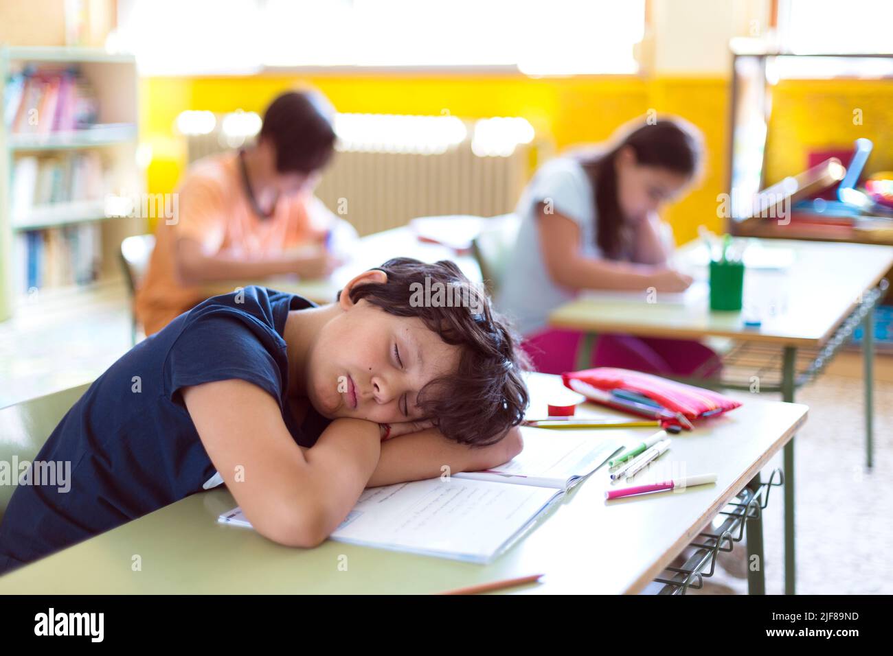 Enfant caucasien dormant en classe pendant que ses camarades de classe font leurs devoirs. Banque D'Images