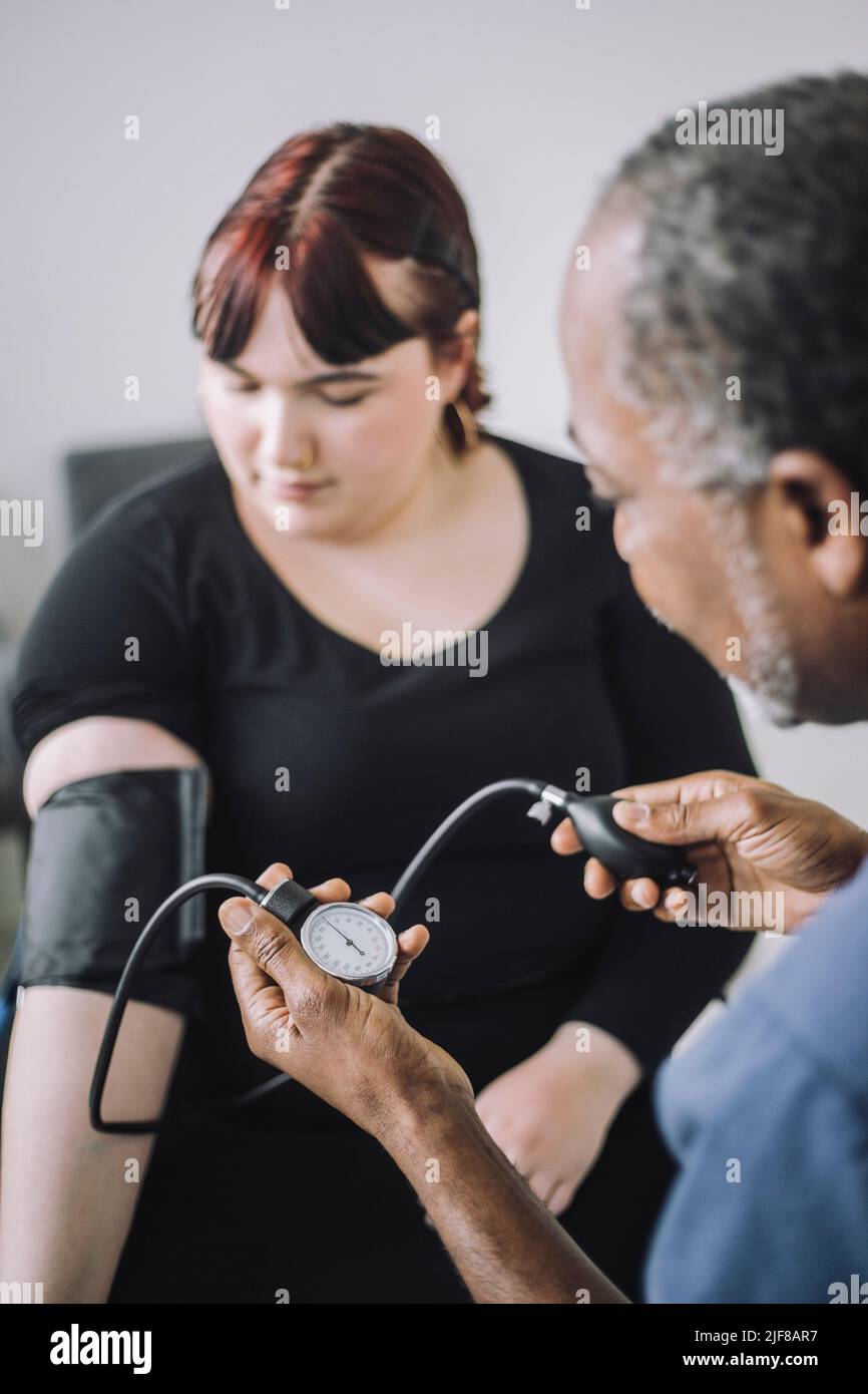 Expert en soins de santé de sexe masculin examinant la pression artérielle d'une patiente en clinique médicale Banque D'Images