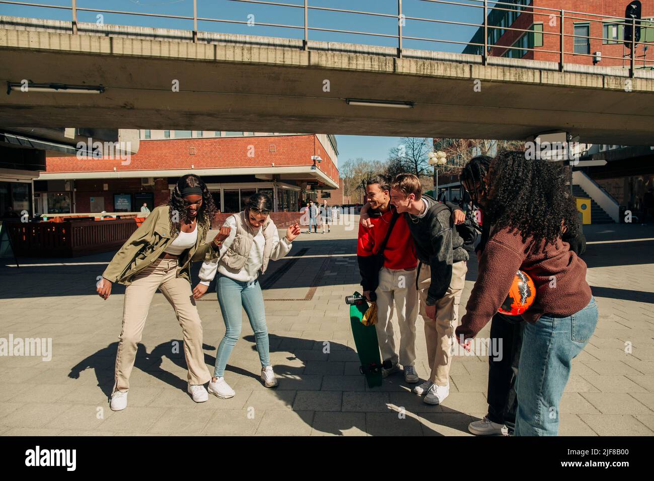 Des amis multiraciaux regardant des jeunes femmes danser ensemble dans la rue pendant la journée ensoleillée Banque D'Images