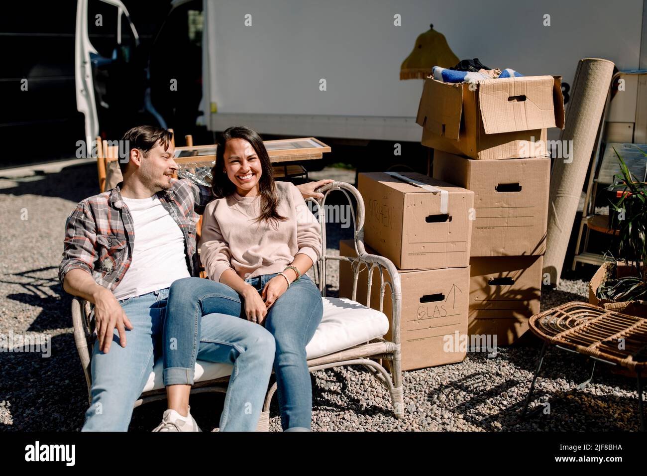Couple souriant assis sur une chaise tout en déménageant dans une nouvelle maison Banque D'Images