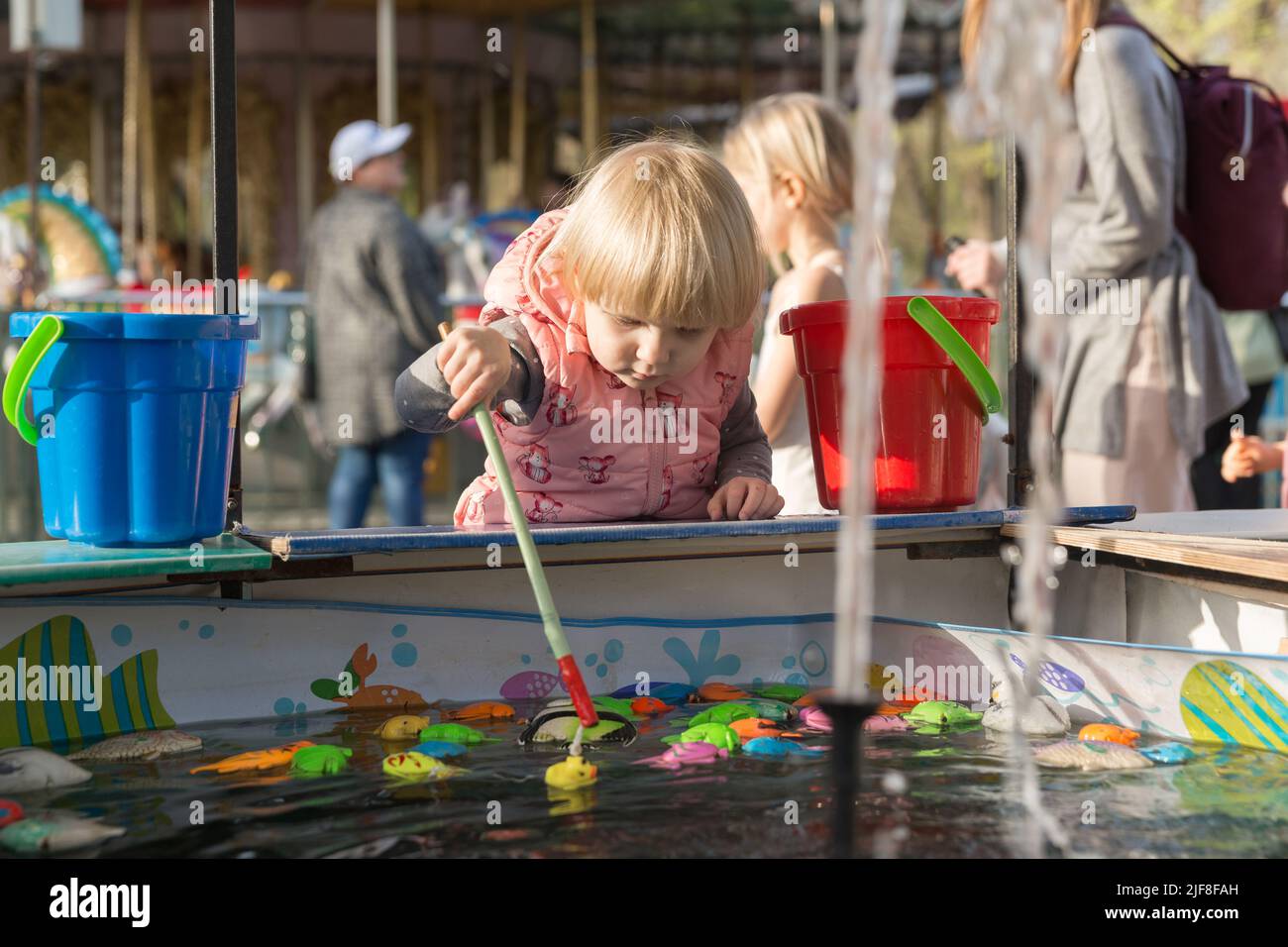 Une fille sérieuse dans un parc municipal joue à la pêche avec une canne à pêche magnétique et des jouets Banque D'Images