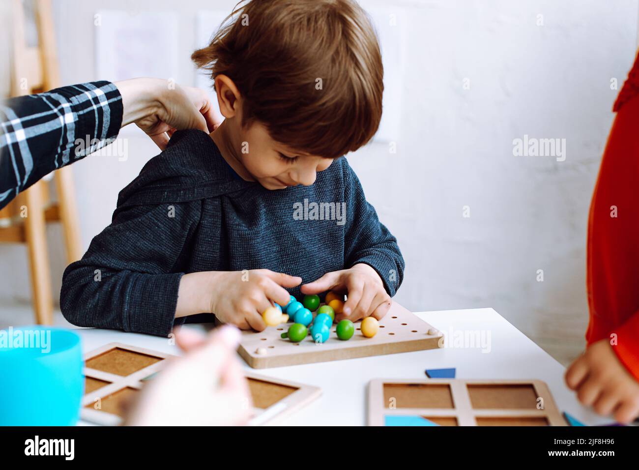 Joli petit garçon pliant des détails colorés de constructeur sur le bureau dans la salle de jeu de près. Jeu intéressant pour les jardins d'enfants de développer la logique et Banque D'Images