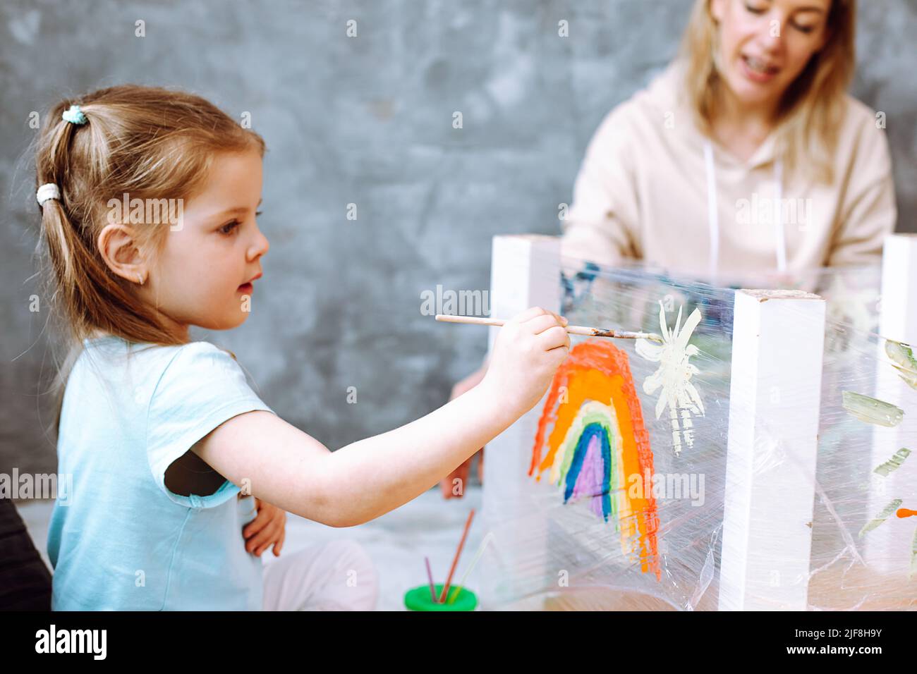 Femme éducatrice menant une leçon avec des enfants dans le dessin à la maternelle. Fille assise et peinture tenant dans le pinceau à la main dans la salle de jeux. Enfants Banque D'Images