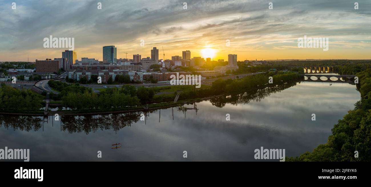 Vue aérienne du centre-ville du Nouveau-Brunswick et de l'université Rutgers tandis que le soleil se couche derrière les édifices de la haute élévation et se reflète sur la rivière Raritan Banque D'Images