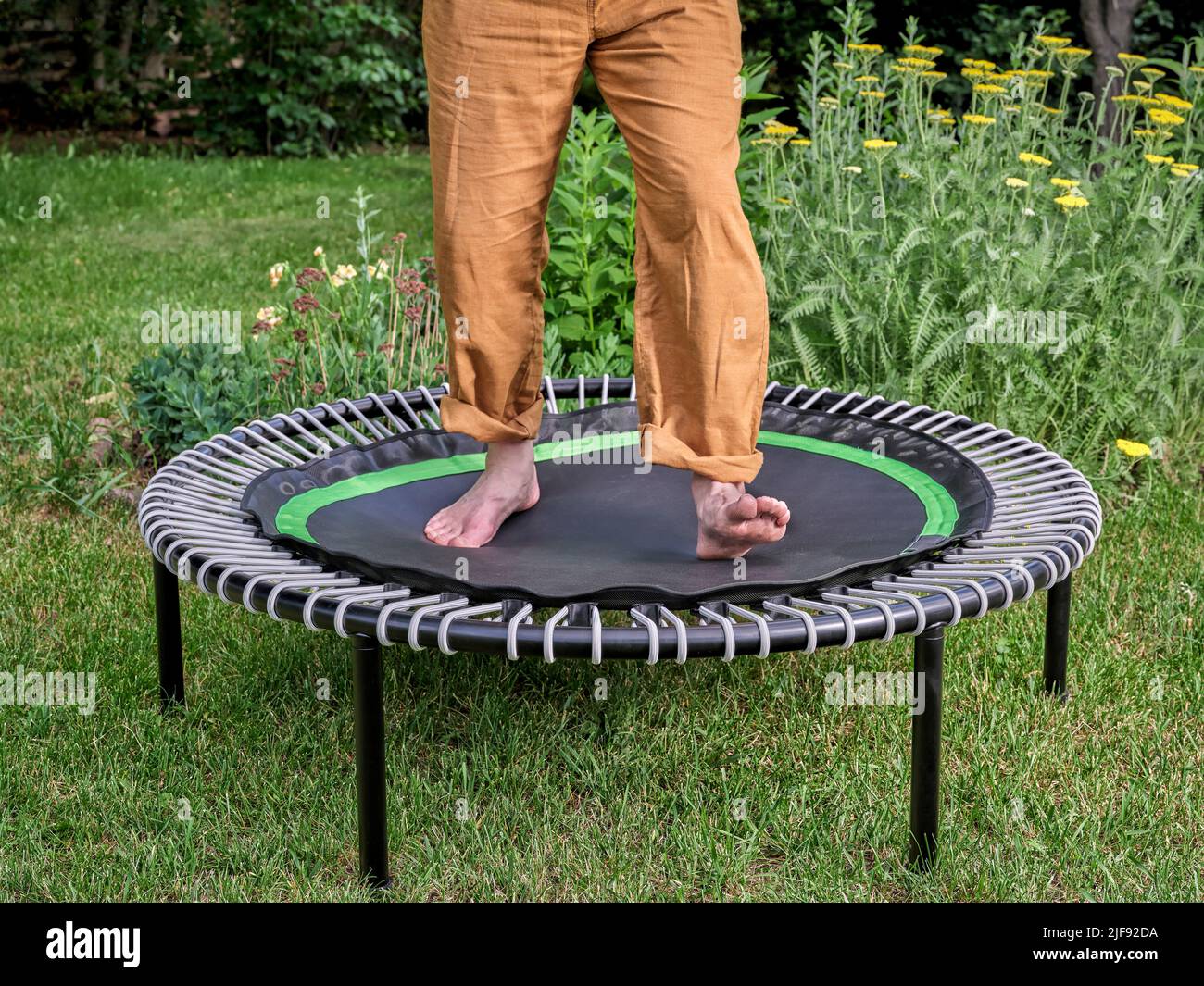 concept de rebond - pieds et jambes d'un homme portant un pantalon de yoga sautant sur un mini trampoline dans une cour Banque D'Images