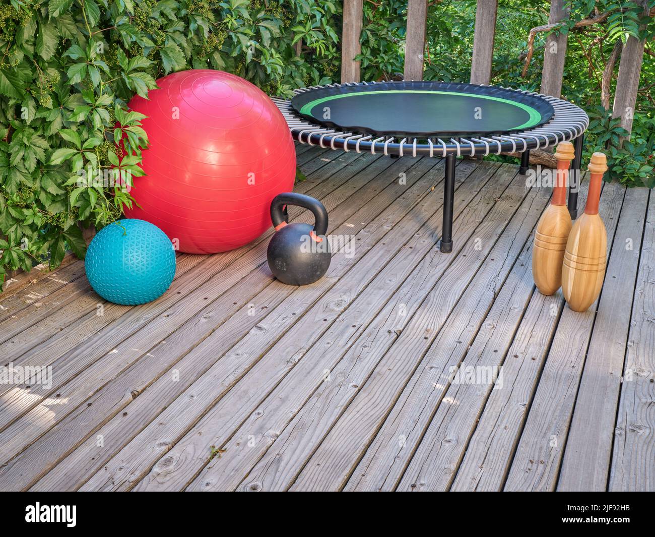 Home Gym concept - slam et balles suisses, kettlebell en fer, mini trampoline et clubs indiens en bois sur un patio arrière-cour Banque D'Images
